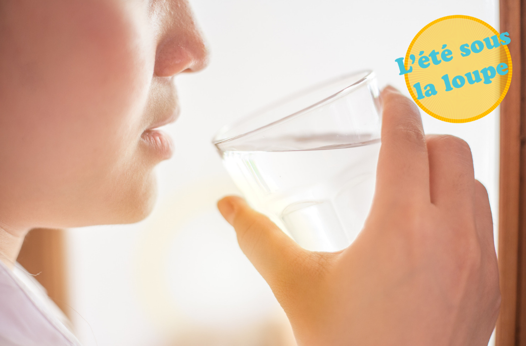 Une personne boit un verre d'eau en regardant le soleil par une fenêtre.