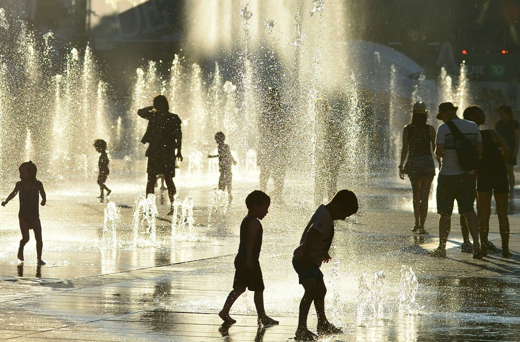 Des enfants jouent avec des jets d'eau au centre-ville de Montréal.