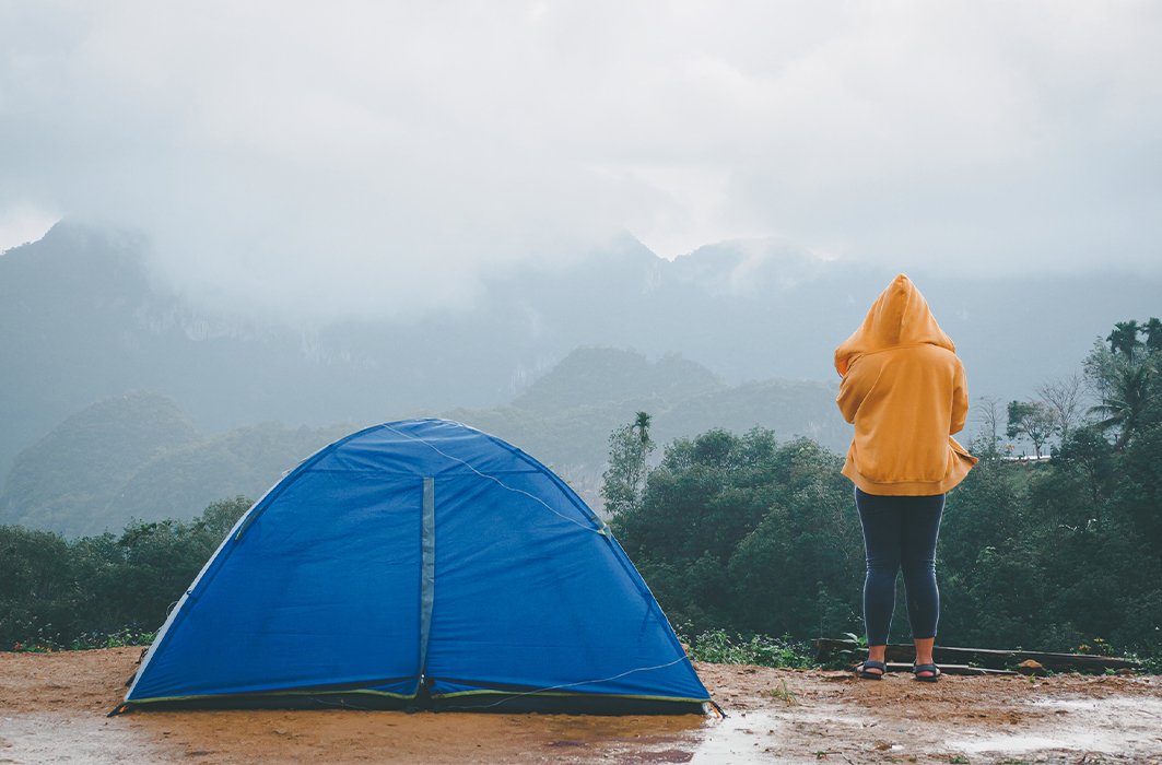 Une personne se tient debout près de sa tente lors d'une journée pluvieuse.