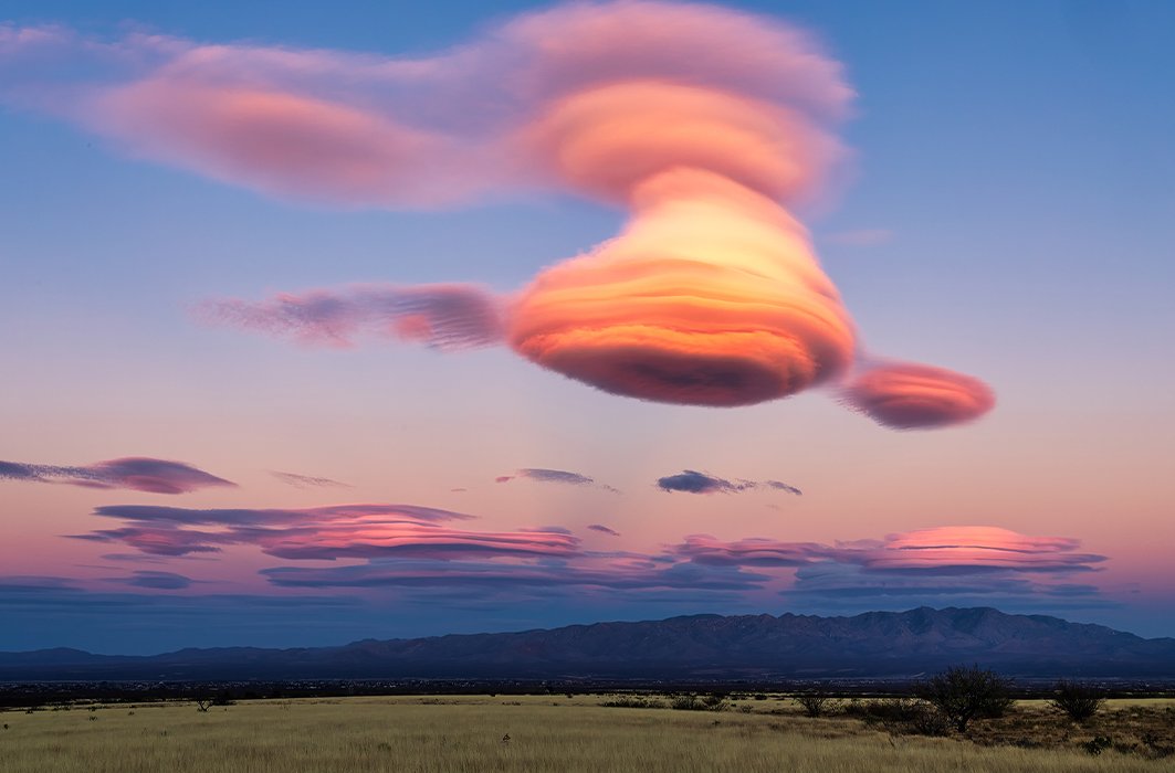 Un paysage avec un nuage lenticulaire au dessus d'une chaine de montagne.